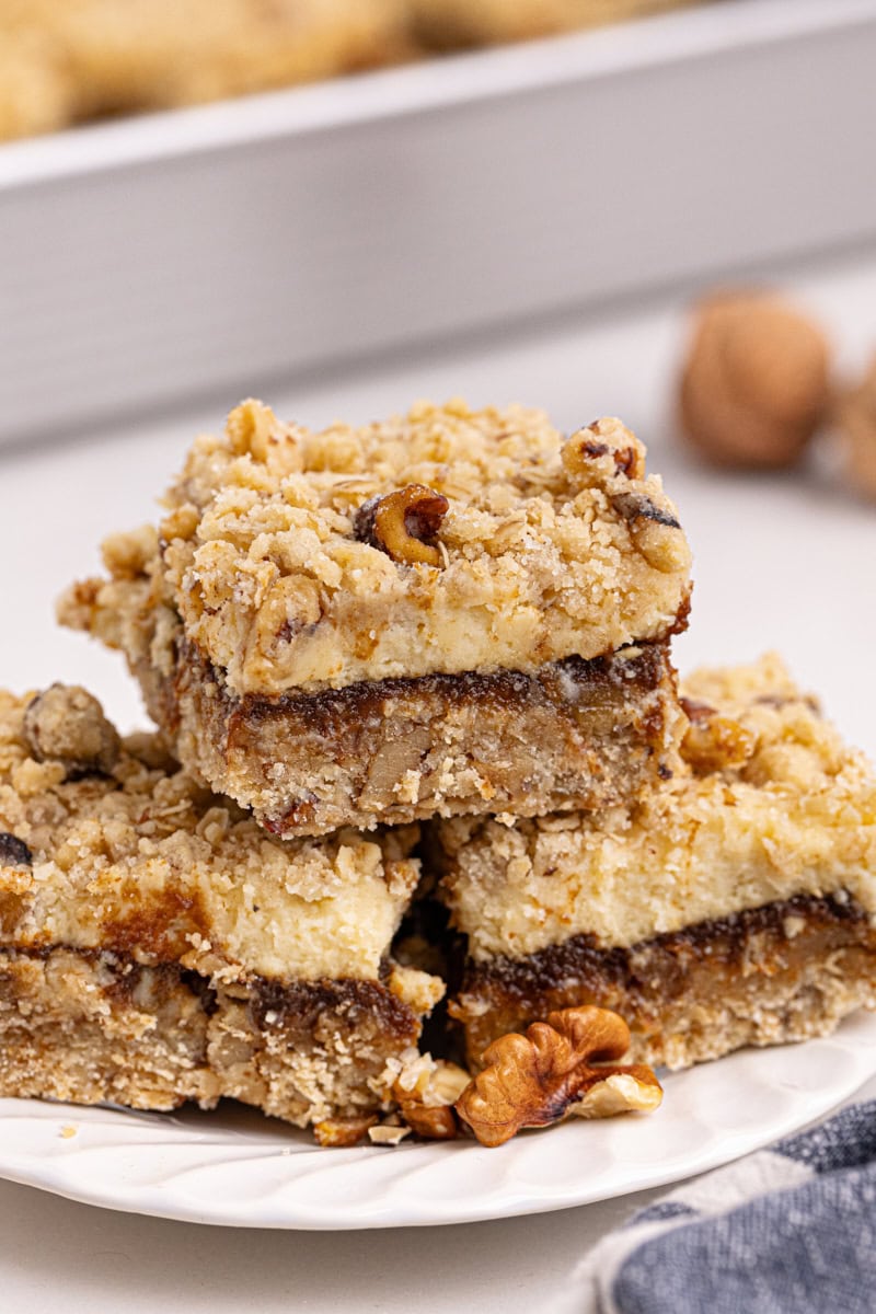 three apple butter cream cheese oat bars stacked on a plate with remaining bars in the background