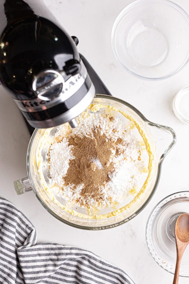 overhead view of confectioners' sugar, cream, chai spice blend, vanilla, and salt added to beaten butter in the bowl of a stand mixer