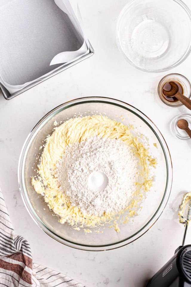 overhead view of flour added to creamed butter and sugar in a glass mixing bowl