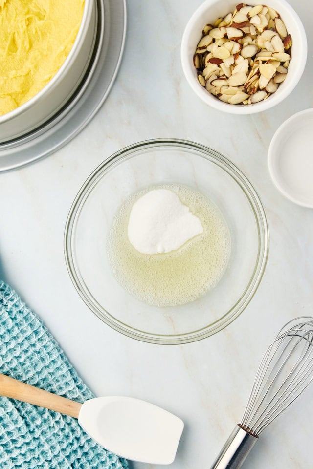 overhead view of sugar added to egg white in a glass bowl