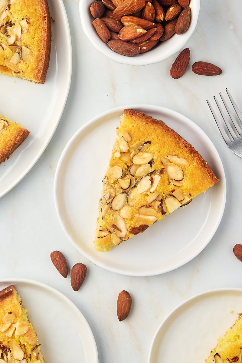 overhead view of a slice of almond torte on a white plate with more cake surrounding