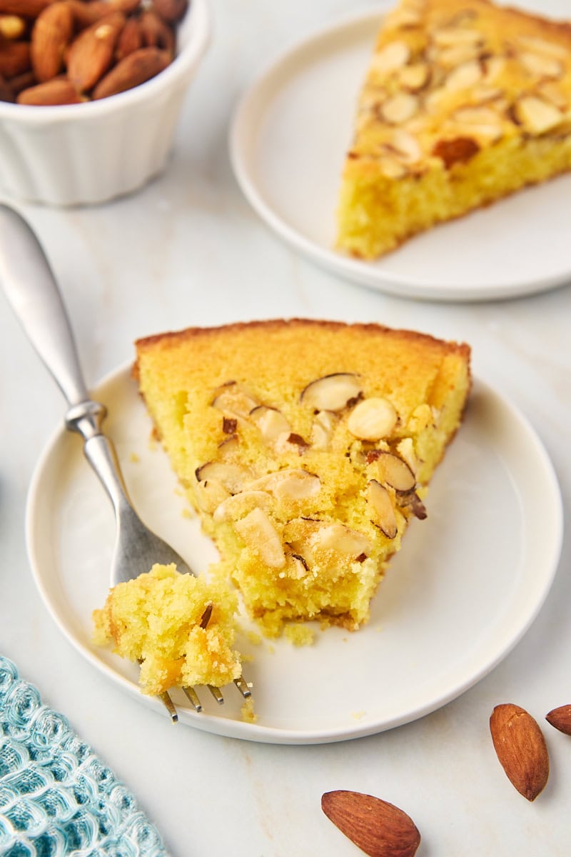 a slice of almond torte on a white plate with a bite on a fork