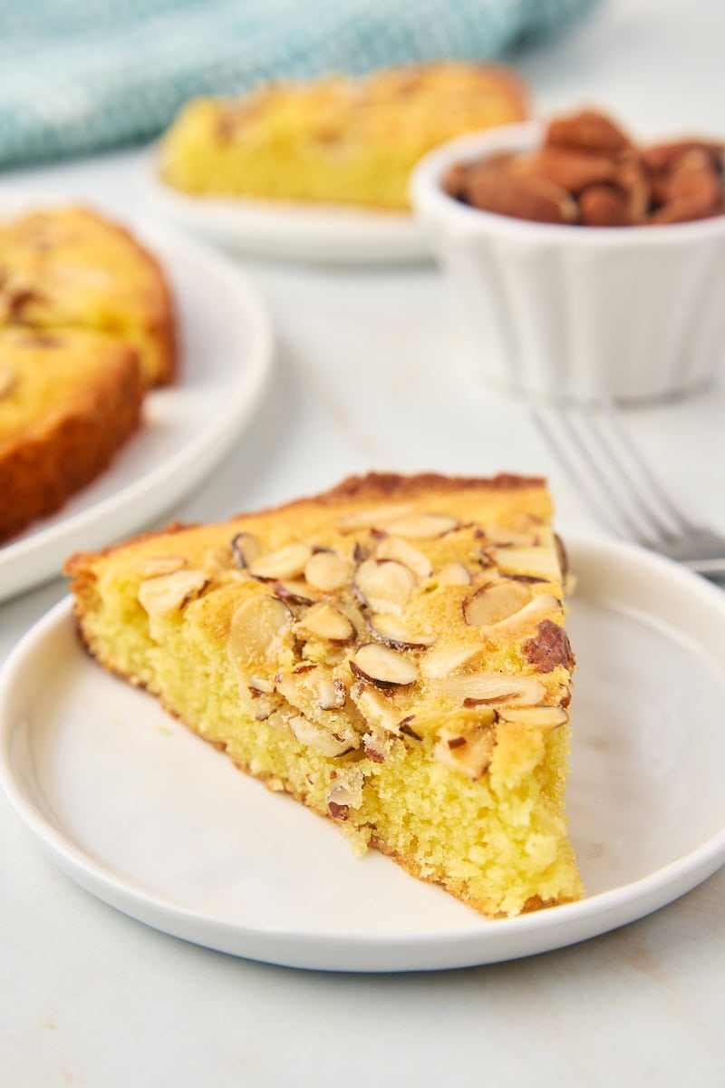 a slice of almond torte on a white plate with more cake in the background