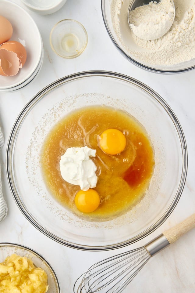 overhead view of eggs, yogurt, and vanilla extract added to banana bread batter