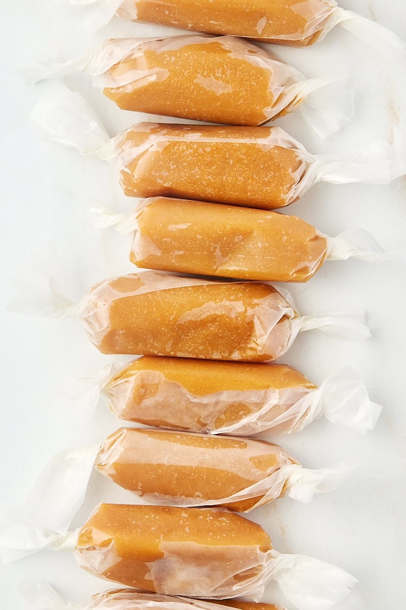 homemade soft caramels wrapped in wax paper, lined up on a marble countertop