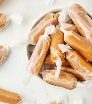 overhead view of homemade soft caramels in a white bowl with more caramels scattered around the bowl