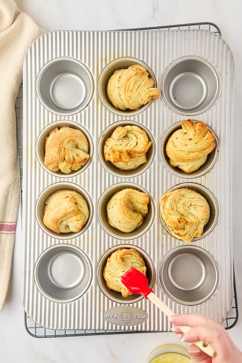 overhead view of melted butter being brushed over freshly baked garlic butter cruffins