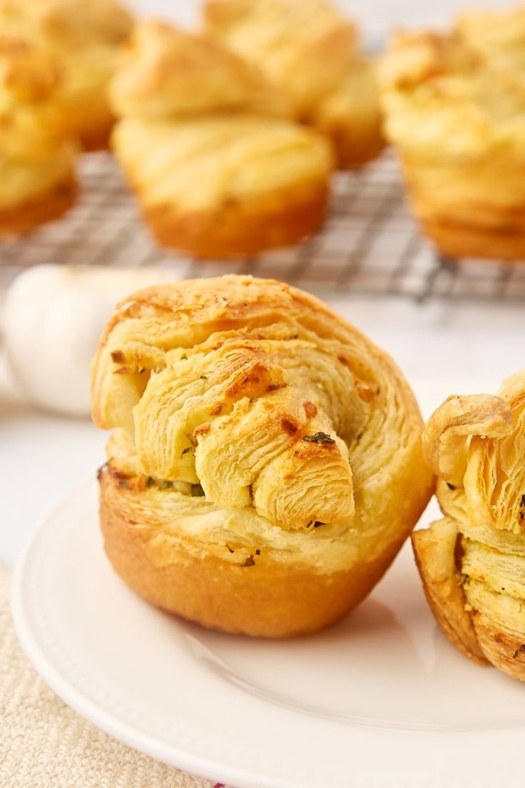 a garlic butter cruffin on a white plate with more cruffins on a wire rack in the background