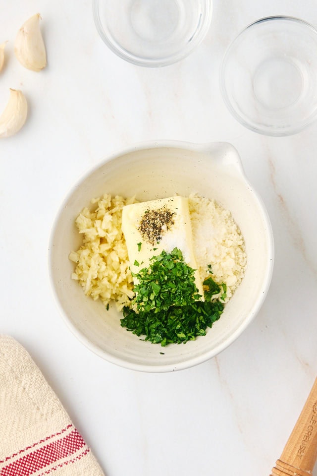 overhead view of butter, garlic, parsley, cheese, salt, and pepper in a small bowl