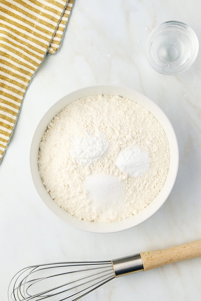 overhead view of flour, baking powder, baking soda, and salt in a glass mixing bowl