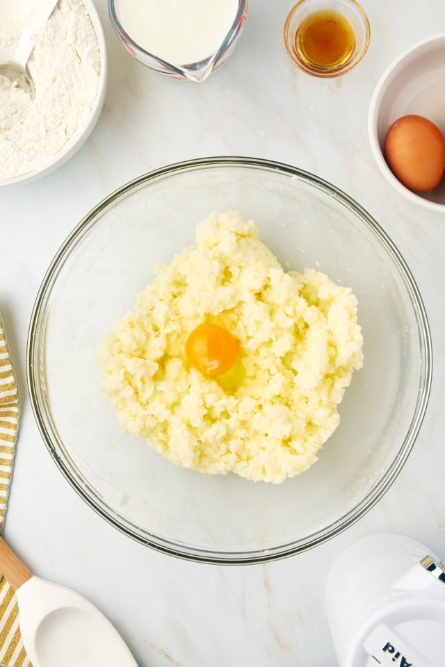 overhead view of egg added to creamed butter and sugar in a glass mixing bowl