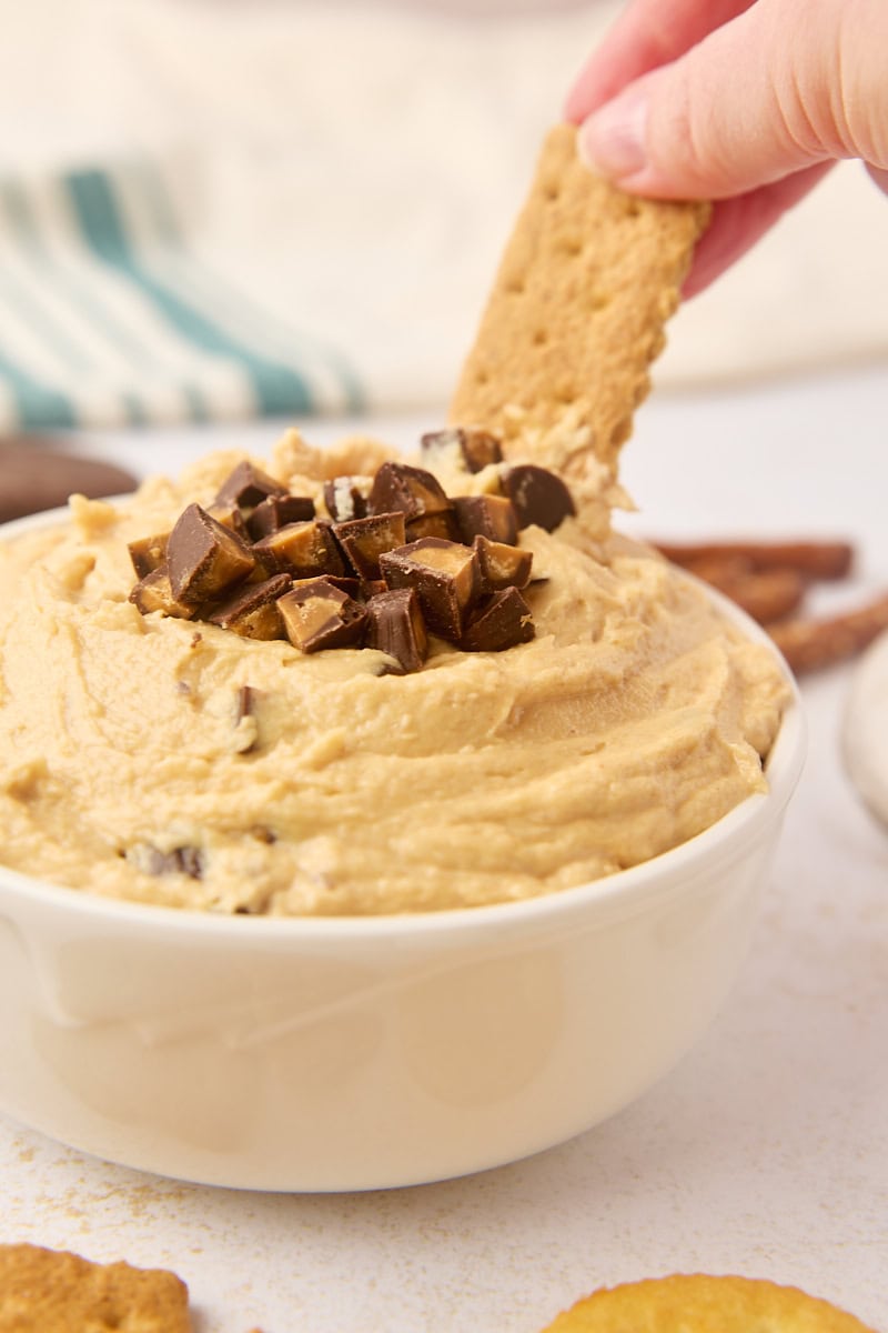 a graham cracker being dipped into peanut butter cup dip