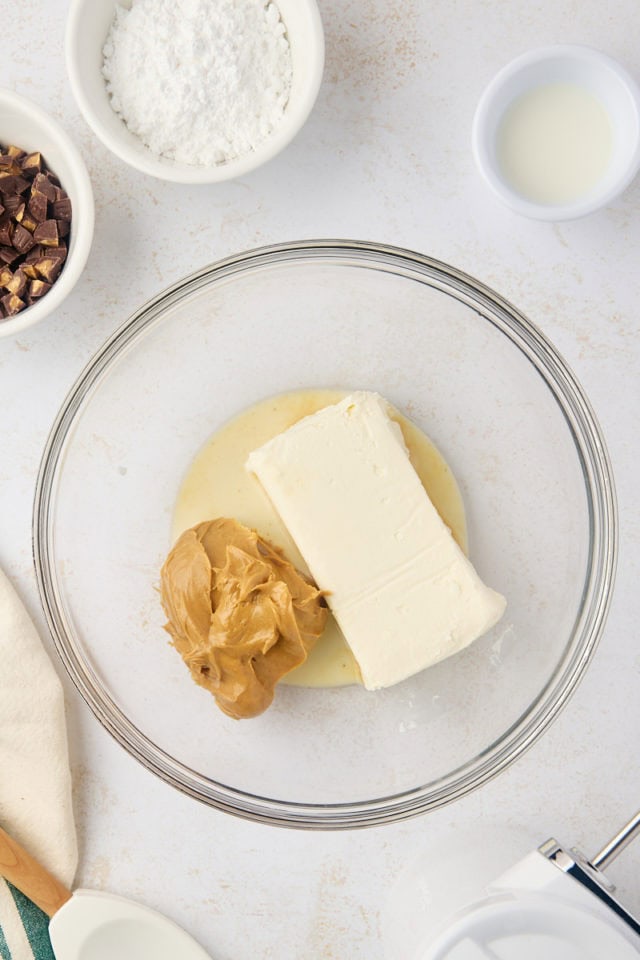 overhead view of cream cheese peanut butter, and milk in a glass mixing bowl