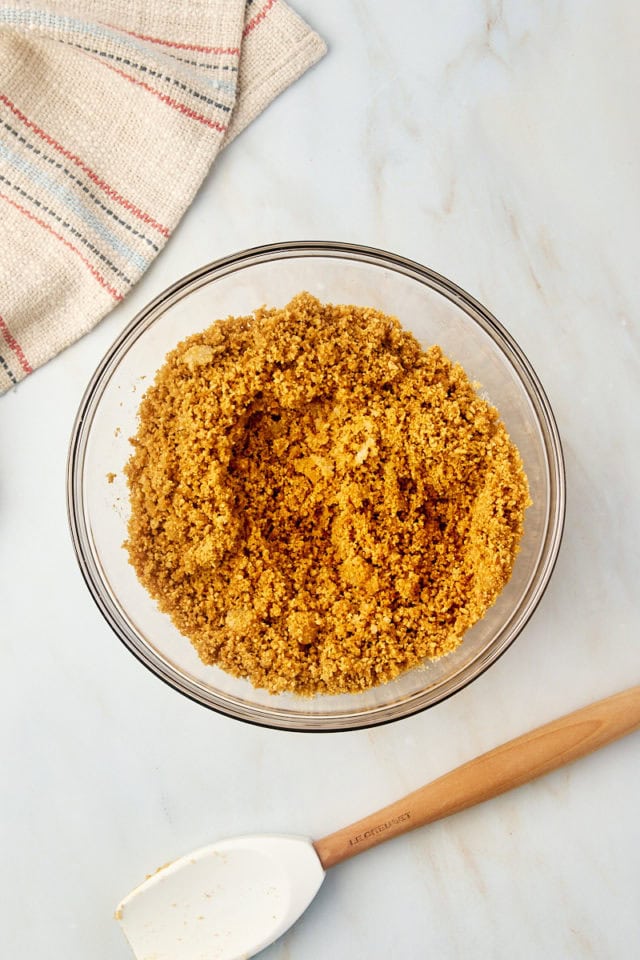 overhead view of mixed graham cracker crust mixture in a glass mixing bowl