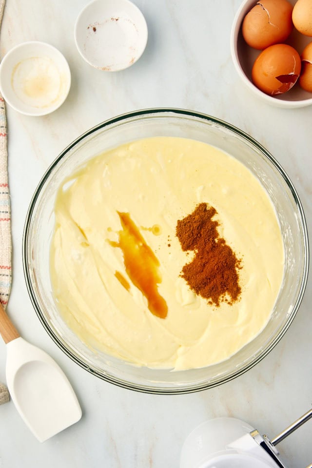 overhead view of cinnamon and vanilla extract added to cheesecake filling