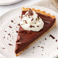 a slice of chocolate mascarpone tart topped with whipped cream and chocolate shavings