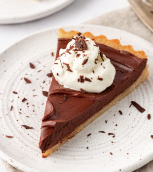 a slice of chocolate mascarpone tart topped with whipped cream and chocolate shavings