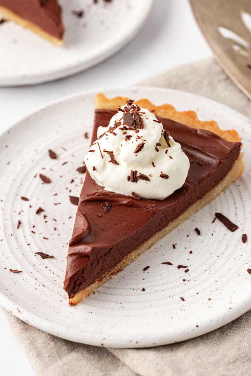 a slice of chocolate mascarpone tart topped with whipped cream and chocolate shavings