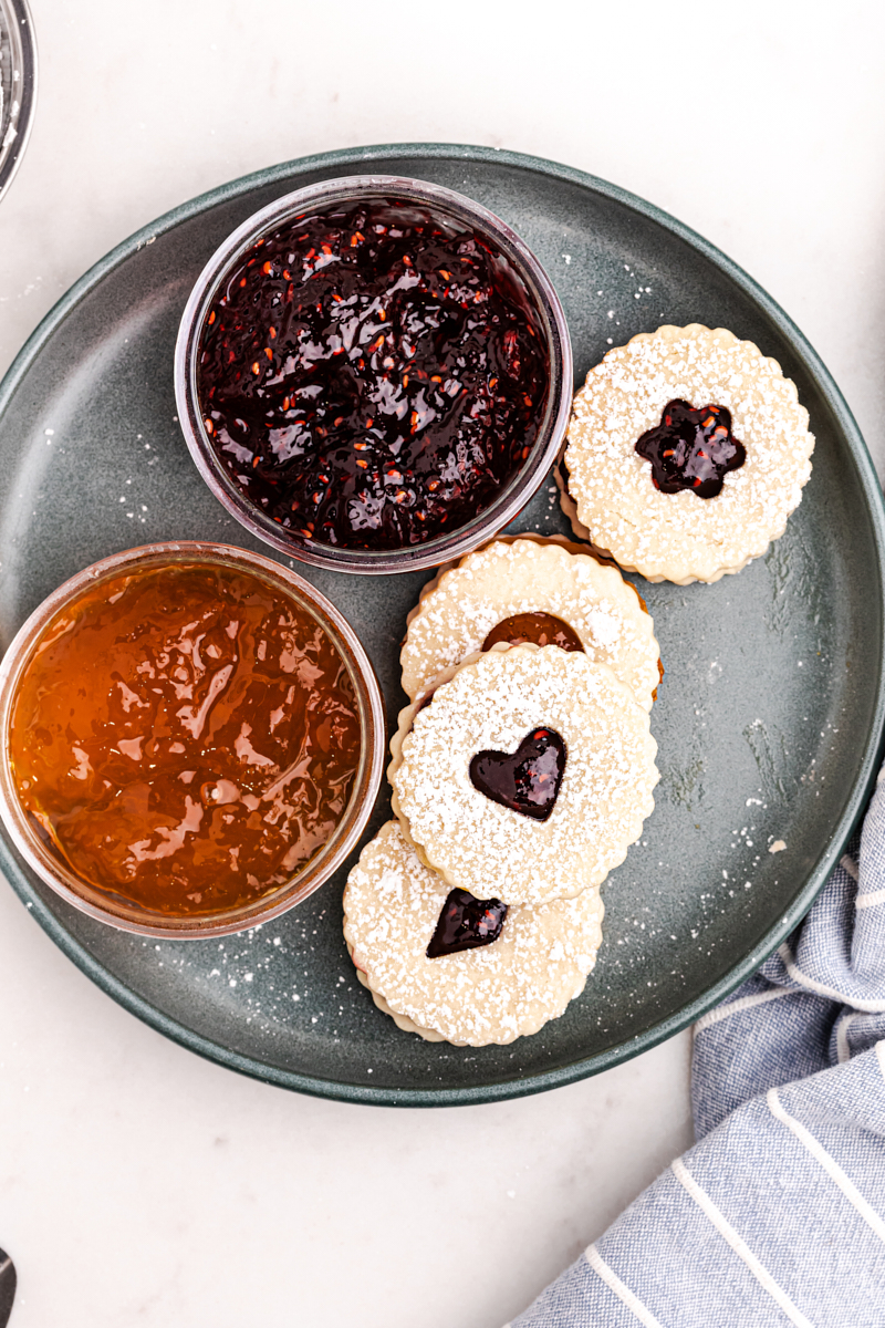 overhead view of four Linzer cookies on a large plate wth two bowls of jam