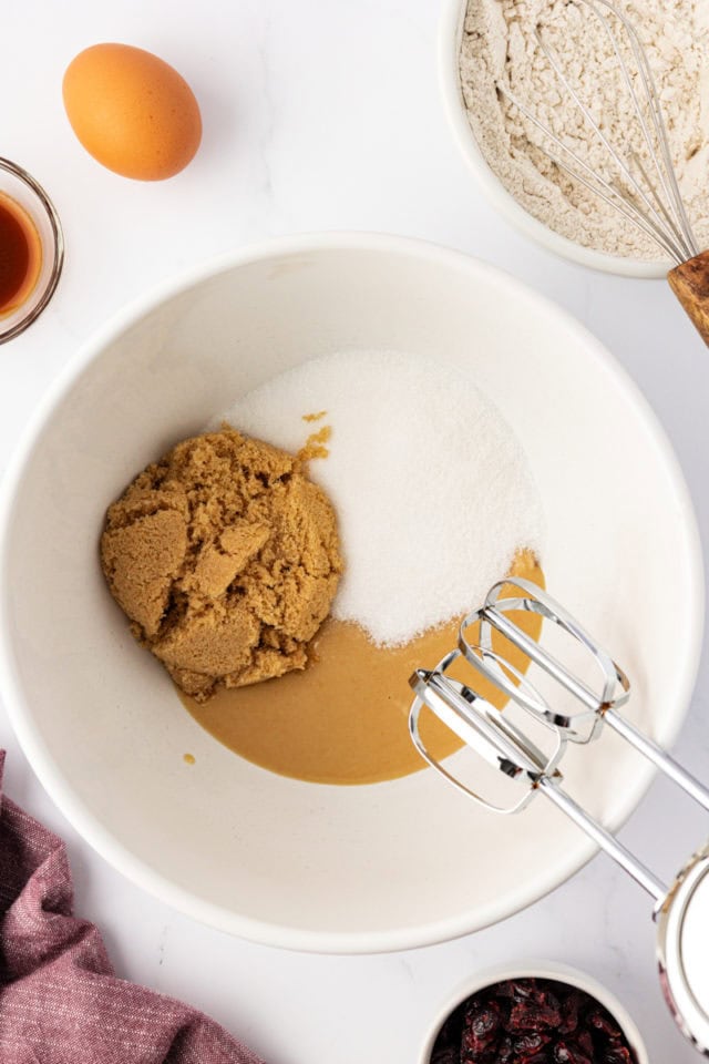 overhead view of macadamia butter, sugar, and brown sugar in a white mixing bowl