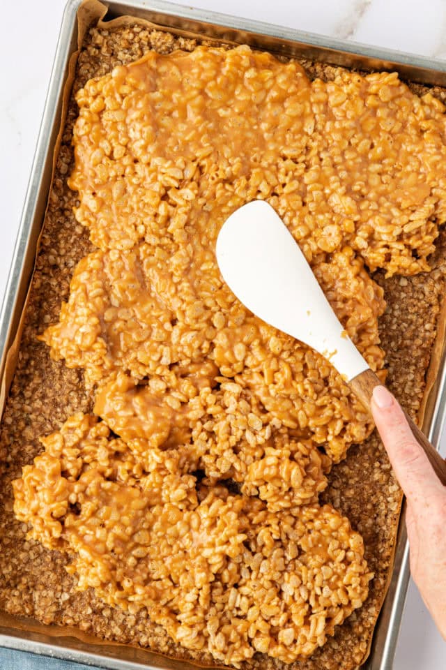 overhead view of peanut butter filling being spread over oat crust for chocolate peanut butter cereal bars