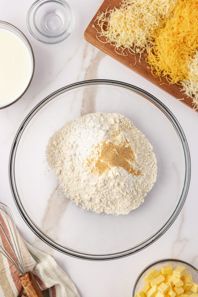 overhead view of flour, baking powder, baking soda, salt, and garlic powder in a glass mixing bowl