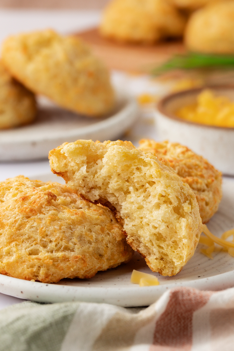 half of a three cheese biscuit on a plate with two more biscuits