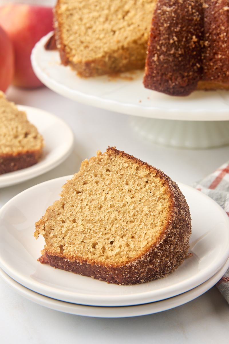 a slice of apple cider donut cake on a white plate with more cake in the background