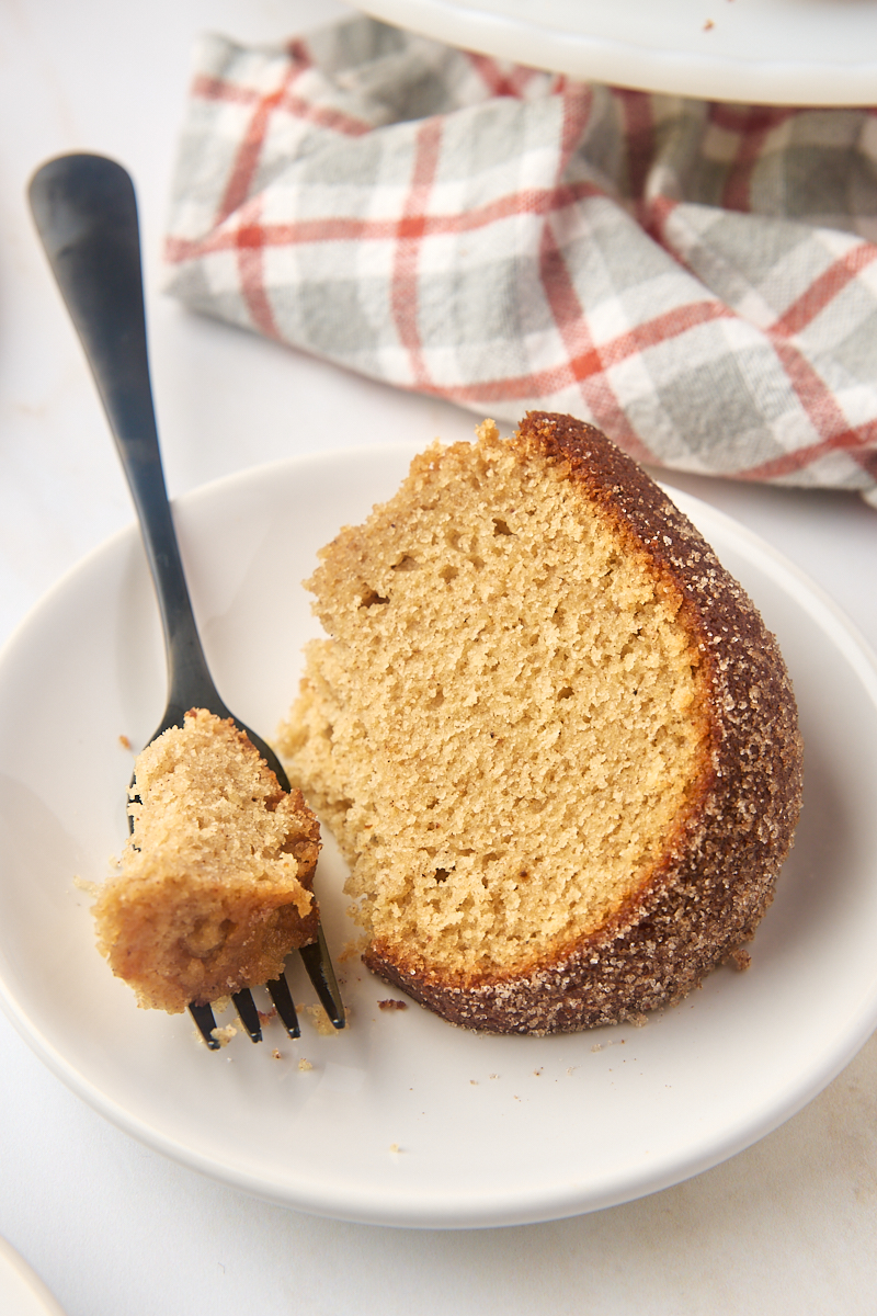 a slice of apple cider donut cake on a white plate with a bite on a fork