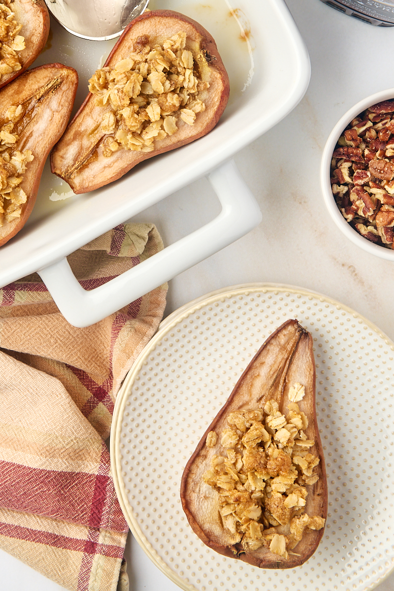 overhead view of a baked pear on a plate with more pears in the baking pan