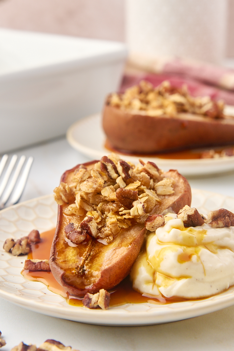 a baked pear on a plate with Greek yogurt, maple syrup, and toasted nuts