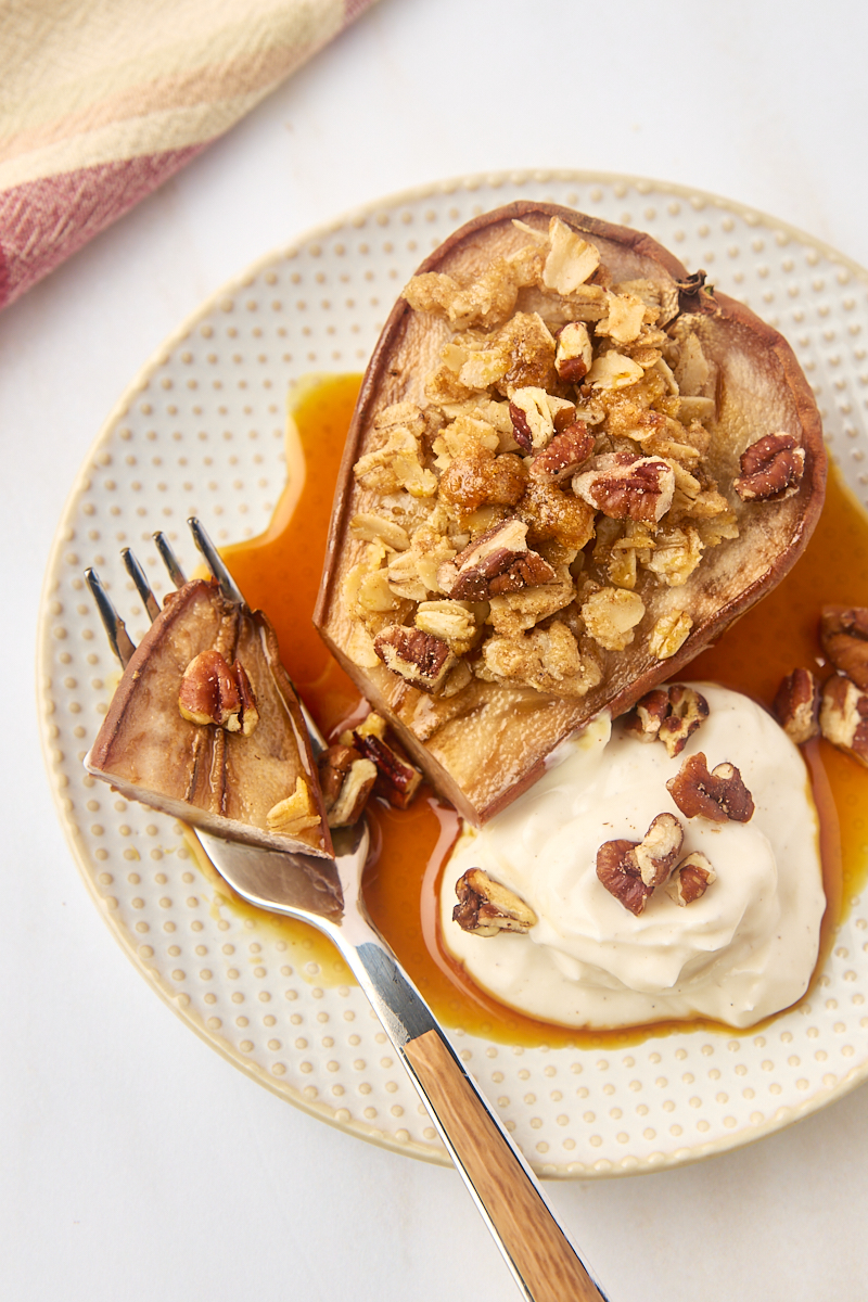 overhead view of a baked pear on a plate with a bite on a fork