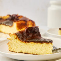 a slice of basque cheesecake on a white plate with more cheesecake in the background