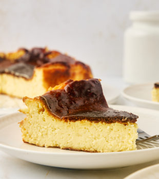 a slice of basque cheesecake on a white plate with more cheesecake in the background