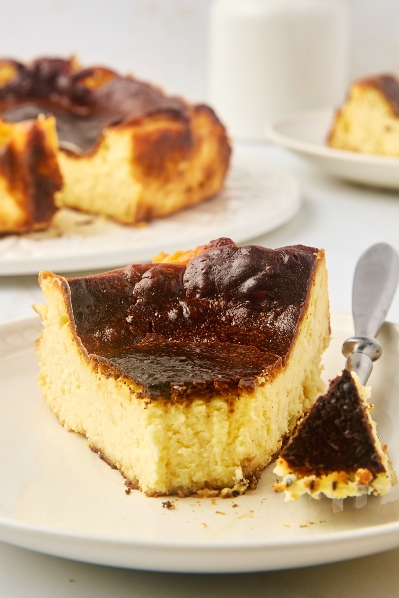 a slice of basque cheesecake on a plate with a bite on a fork