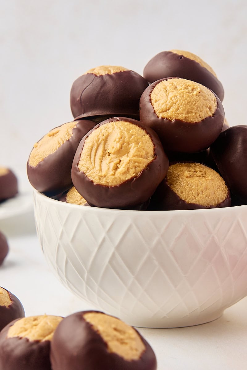 buckeyes in a white bowl with more buckeyes surrounding