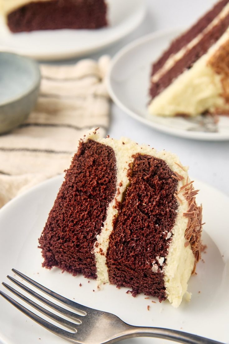 a slice of mahogany cake on a white plate with more cake in the background