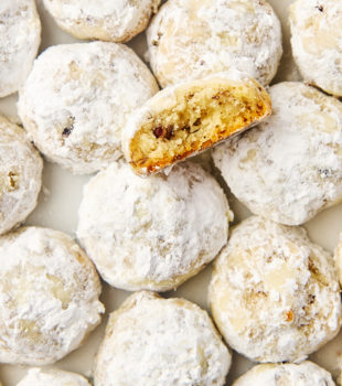 overhead view of snowball cookies on parchment with a partial cookie on top