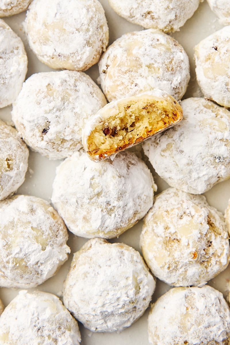 overhead view of snowball cookies on parchment with a partial cookie on top