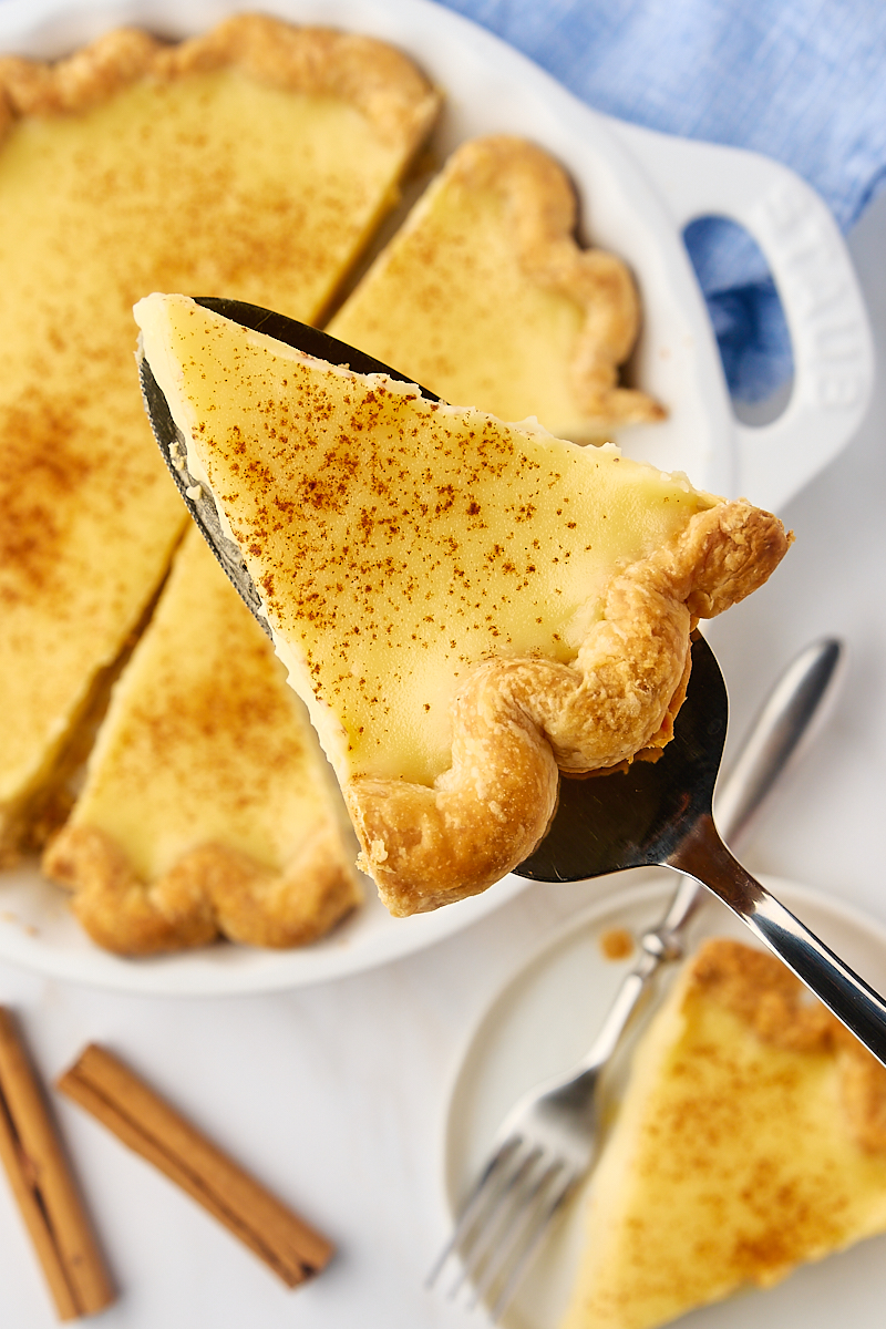 overhead view of a slice of sugar cream pie on a pie server held over the remaining pie