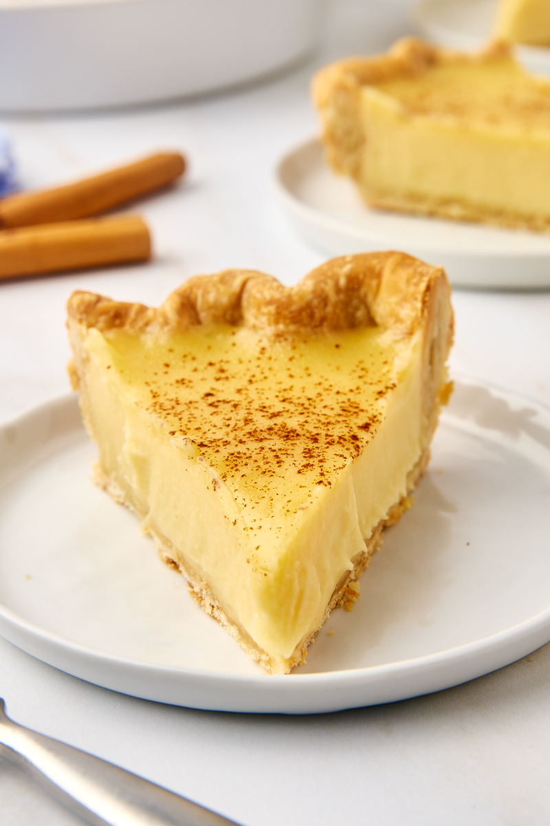 a slice of sugar cream pie on a white plate with more pie in the background