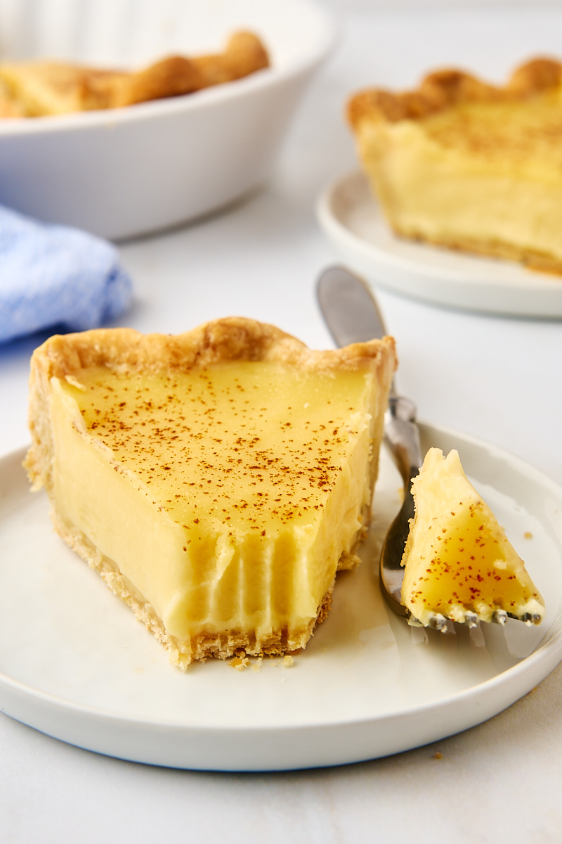 a slice of sugar cream pie on a white plate with a bite on a fork