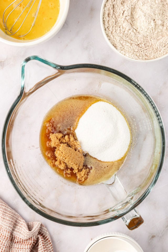 overhead view of sugar and brown sugar added to brown butter in a mixing bowl