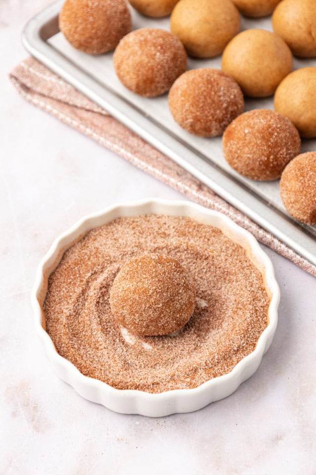 a brown butter snickerdoodle cookie dough ball being rolled in cinnamon-sugar