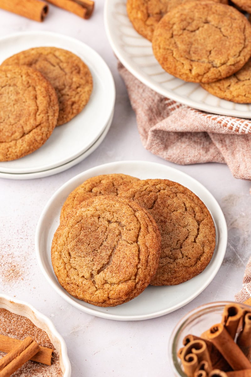 three brown butter snickerdoodles on a white plate with more cookies surrounding