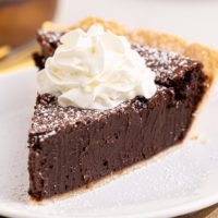 a slice of hot fudge pie topped with powdered sugar and whipped cream