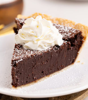 a slice of hot fudge pie topped with powdered sugar and whipped cream