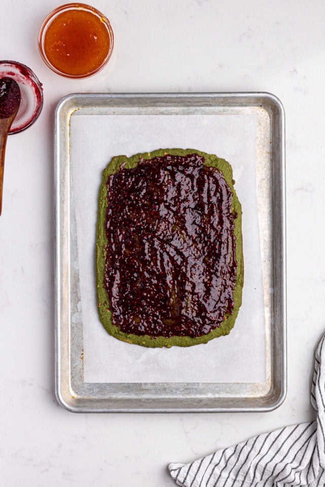 overhead view of raspberry preserves spread on green layer of Italian rainbow cookies