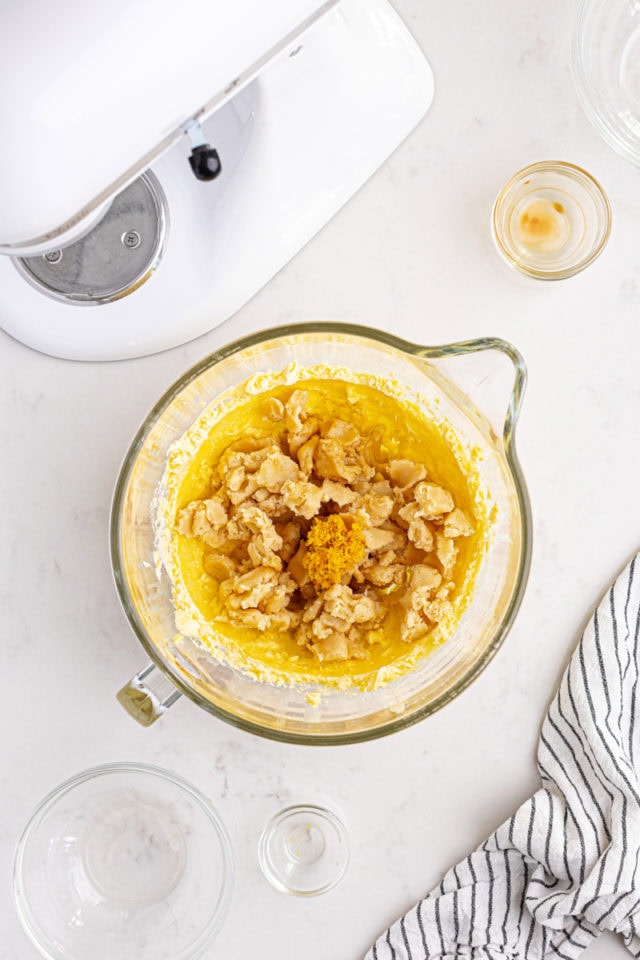 overhead view of almond paste, almond extract, vanilla extract, and orange zest added to creamed butter and sugar