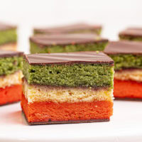 an Italian rainbow cookie on a small white pedestal with more cookies behind